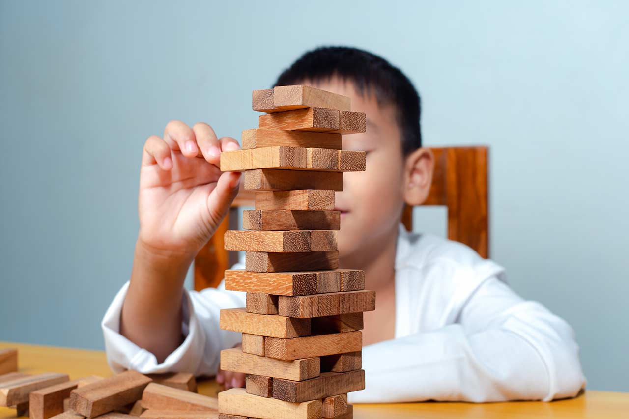 Junge spielt mit einem Wackelturm aus Holz